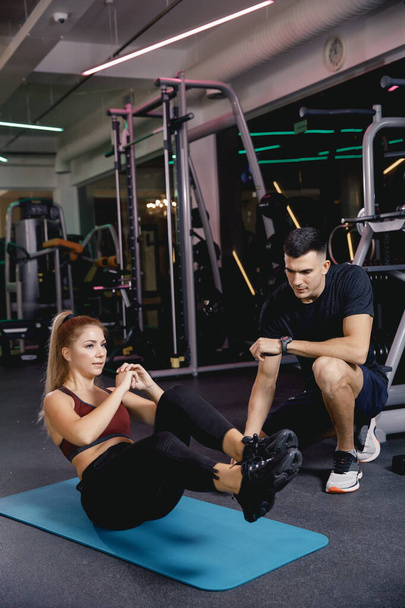 The male coach helps to do the exercise. The girl is engaged in sports with a mentor. Athletes practice in the gym. exercise for the press. - Foto, Imagem
