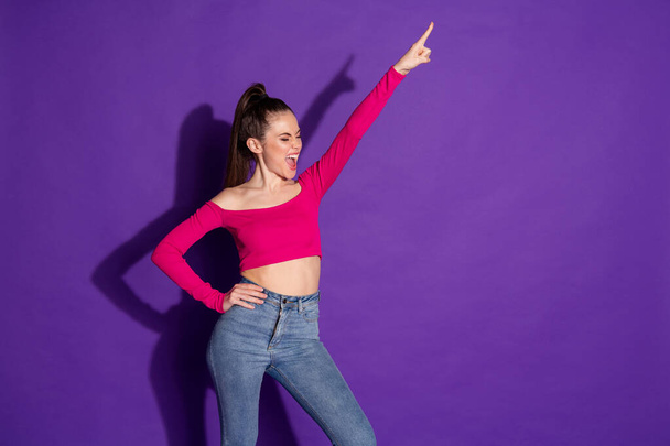 Photo of crazy young lady raise arm pointing finger up shout wear jeans pink uncovered shoulders top isolated purple color background - Fotografie, Obrázek