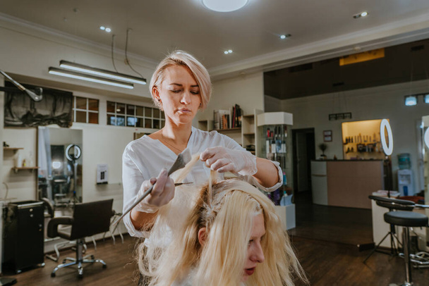 Профессиональный парикмахер окрашивает волосы клиентки с светлыми волосами в салоне красоты - Фото, изображение