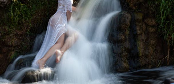 Soft focus blurred image of seminude young woman in a white dress enjoys the freshness and coolness in the water jets of the waterfall - Zdjęcie, obraz