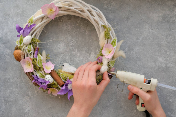 A faceless woman creates an Easter wreath, glues with a glue gun. The concept of the holiday and the spring season. - Photo, Image