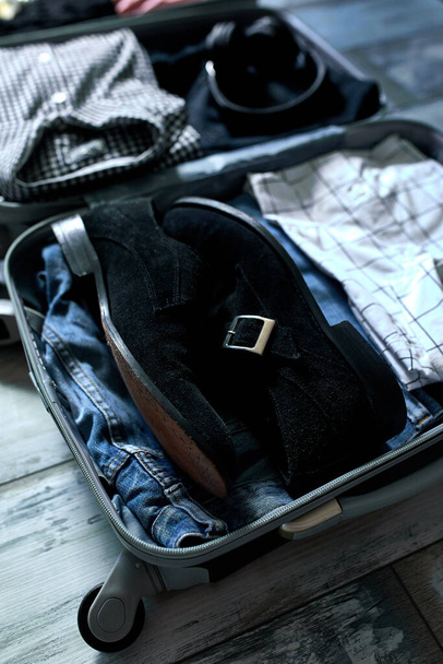 Koffer zu Hause packen mit lässigen Herrenartikeln, Sachen - Jeans, Hemden, Kopfhörer im Koffer für Reisen, Reisen, Urlaub. Kopierraum. - Foto, Bild