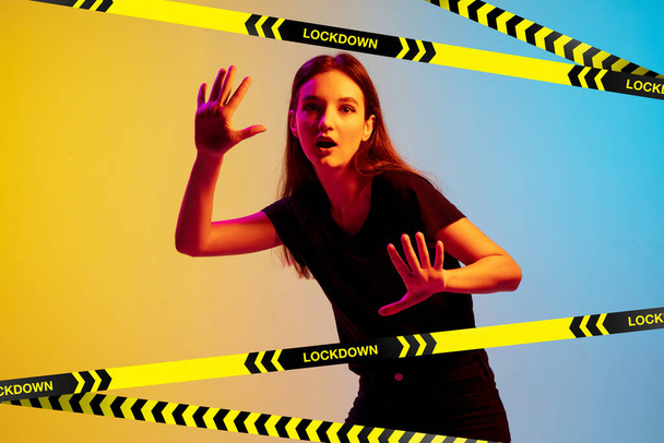 Young sportive woman posing on gradient neon background behind limiting tapes with word Lockdown - Foto, Bild