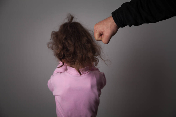 Father beats his daughter, gray background.  - Photo, Image