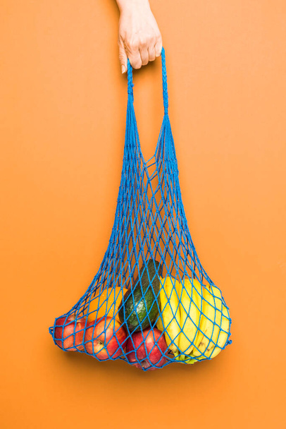 A female hand holds an organic eco mesh bag  with fruits. Zero waste. Recycling concept. - Fotó, kép