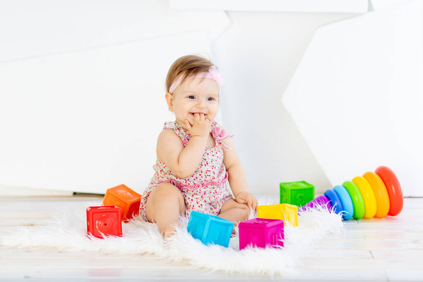 pequeña niña feliz sentada en una habitación blanca en un vestido rojo con juguetes brillantes - Foto, imagen