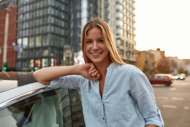 Портрет щасливої молодої кавказької дівчини, що спирається на білу машину
 - Фото, зображення