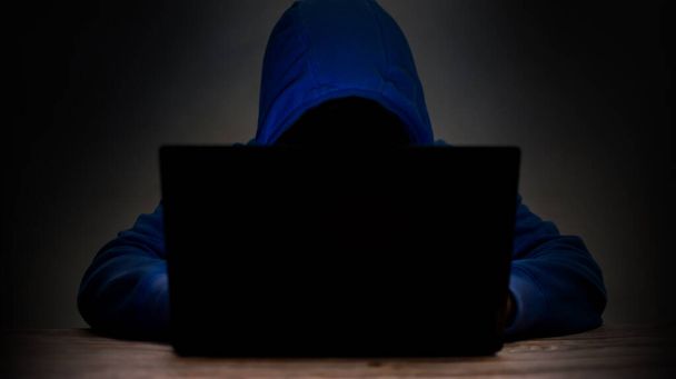 L'uomo indossa una camicia blu con cappuccio davanti a un computer portatile. Hacking idee, furto di computer per danneggiare - Foto, immagini