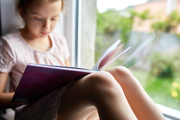 Petite fille mignonne lisant le livre à la maison, au rebord de la fenêtre, Enfant étudiant à la maison, quarantaine, rester à la maison, style de vie. - Photo, image