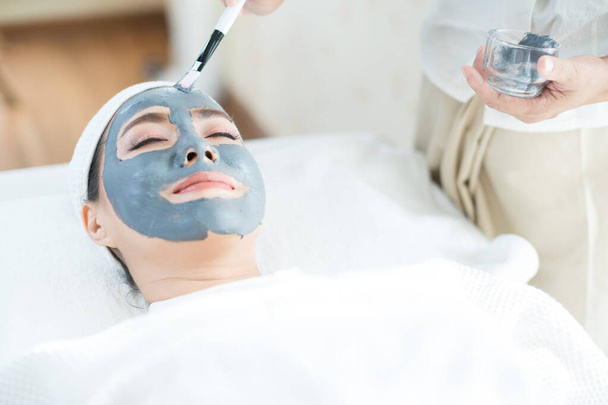 Portret van een vrouw met klei gezichtsmasker in een schoonheidssalon. gelukkig vrouw het hebben van facial in spa salon. - Foto, afbeelding