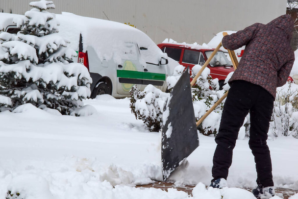 Un hombre quita la nieve de los caminos con una pala especial. Las nevadas agregaron trabajo a los limpiaparabrisas. Limpiando nieve en las aceras con una pala. - Foto, imagen