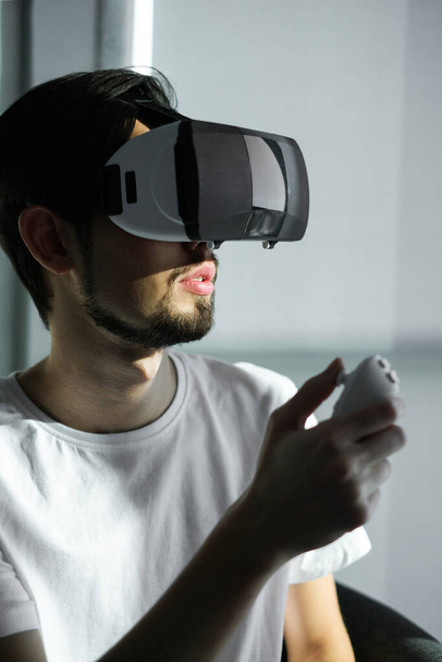 um jovem joga um jogo virtual em óculos VR. lazer em casa sobre auto-isolamento em casa. A realidade virtual. retrato de belo jovem vestindo óculos de realidade virtual - Foto, Imagem