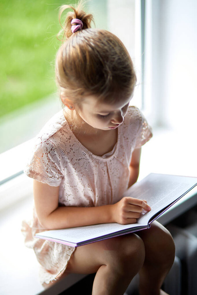 Bonito livro de leitura menina em casa, no peitoril da janela, Criança estudando em casa, quarentena, ficar em casa, estilo de vida. - Foto, Imagem