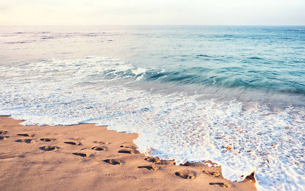 Ślady stóp na piaszczystej plaży tropikalnej o zachodzie słońca, zastosowane tonowanie kolorów. - Zdjęcie, obraz