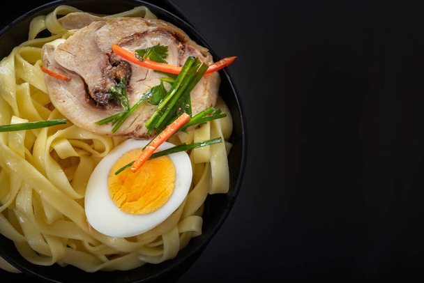 Noodles with pieces of meat and an egg in a black plate on a dark table. View from above. Asian food concept. Copy space. Close-up - Foto, Imagem