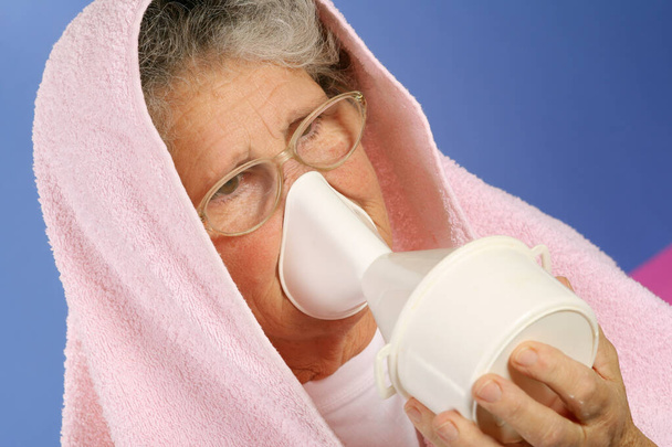 Ältere Frau mit Handtuch über dem Kopf inhaliert ätherischen Öldampf gegen Erkältungen und Halsschmerzen - Foto, Bild