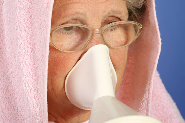 Крупным планом 65-летняя больная женщина использует ингалятор для лечения простуды и боли в горле - Фото, изображение