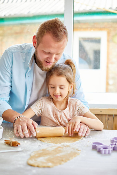 Otec ukazuje své dceři, jak se válí těsto na sušenky, peče v kuchyni, doma vaří.. - Fotografie, Obrázek