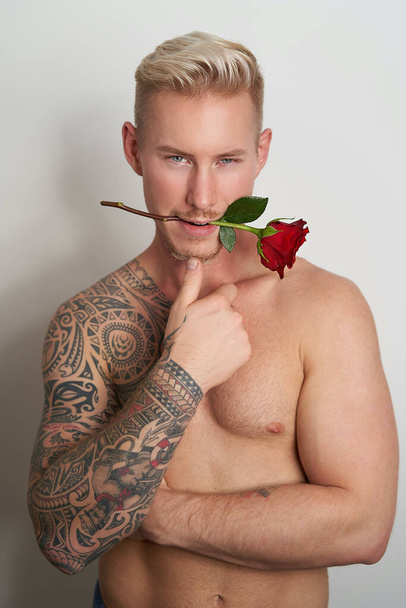 Male lover with a flower in the mouth / Handsome young man holding a red rose in his lips - Foto, Imagem
