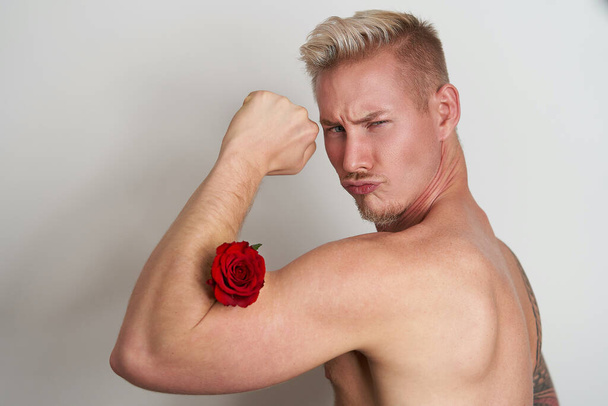 Männlicher Liebhaber lässt Muskeln mit einer Blume spielen / Schöner junger Mann drückt eine rote Rose in seinen Bizeps - Foto, Bild