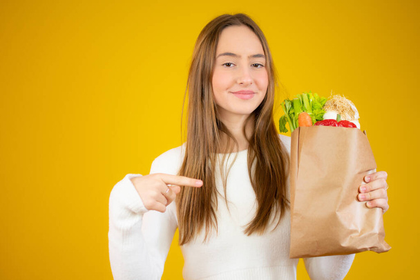 Portret van een mooi tienermeisje met een boodschappentas en een glimlach tegen een gele achtergrond - Foto, afbeelding