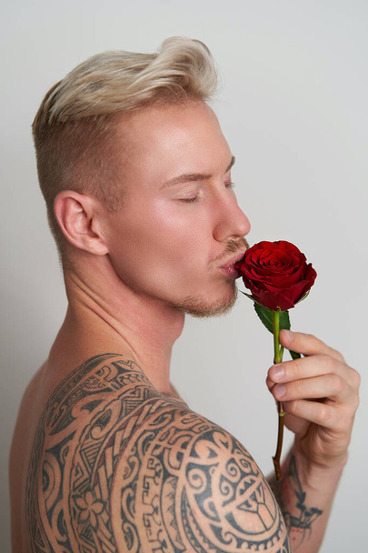 Amante masculino besando una flor / Joven guapo besando una rosa roja en expectativa seductora - Foto, Imagen
