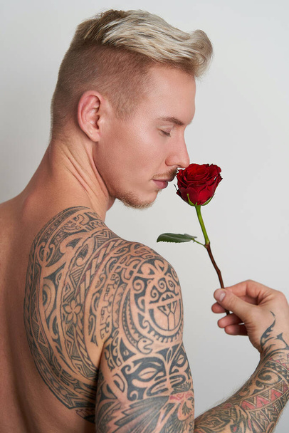 mężczyzna kochanek wąchając a kwiat / przystojny młody człowiek wąchając a czerwony róża w uwodzicielskie oczekiwania - Zdjęcie, obraz
