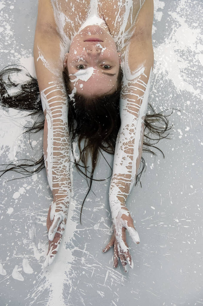 Retrato de uma mulher morena sexy com braços levantados pintados com tinta branca no chão de estúdio cinza, arte de pintura corporal abstrata expressiva criativa, espaço de cópia - Foto, Imagem