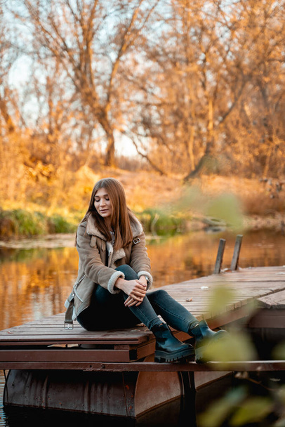 Beautiful woman sitting by the lake and enjoying the beauty of golden autumn - Photo, Image