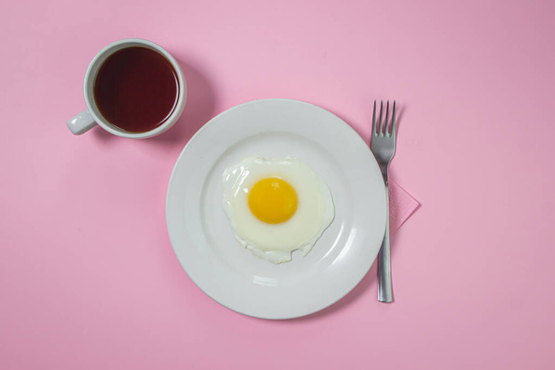 Scrambled eggs on a pink background. Fried eggs on a white plate. Delicious breakfast with a cup of coffee. - Фото, изображение