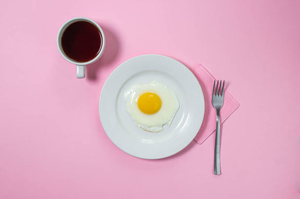 Roerei op een roze achtergrond. Gefrituurde eieren op een wit bord. Heerlijk ontbijt met een kop koffie. - Foto, afbeelding
