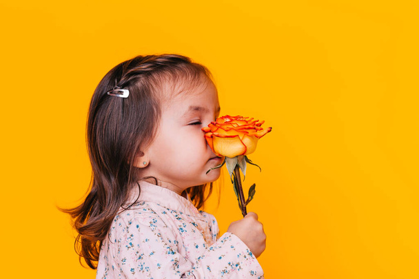 Child holding a flower in front of a yellow background. Valentine's Day. Mother's day. - Foto, Bild