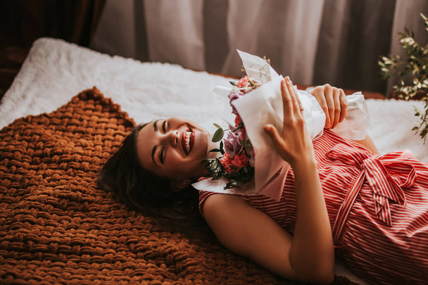 Een vrouw in een wit shirt met een boeket bloemen. Valentijnscadeau. Vrouw op het bed. - Foto, afbeelding