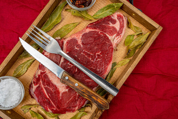 Nyers marhahús borda egy régi fából készült tálcán, sópelyhekkel, cayenne paprikával és babérlevéllel, vörös ronggyal a hátán. Ínyenc élelmiszer-koncepció - Fotó, kép