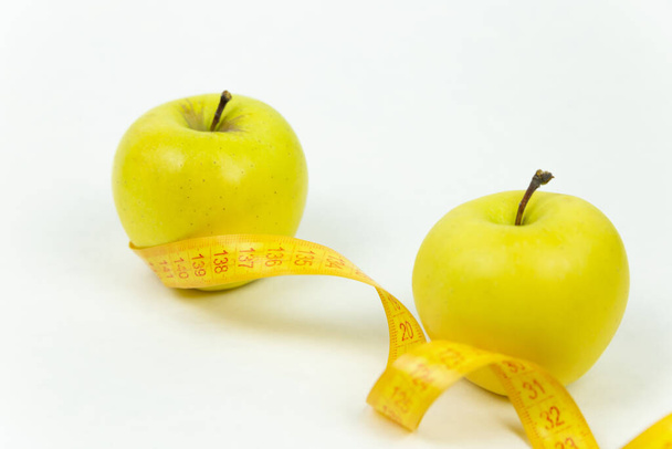 Měřicí páska omotaná kolem dvou zelených jablek jako symbol stravy. Koncept zdravého životního stylu, jídla a sportu, na bílém pozadí. Boční pohled s mezerou pro kopírování. - Fotografie, Obrázek