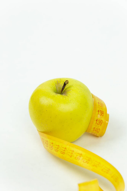 Taśma pomiarowa owinięta wokół zielonego jabłka jako symbol diety. Koncepcja zdrowego stylu życia, żywności i sportu, na białym tle. Widok boczny z przestrzenią do kopiowania. - Zdjęcie, obraz