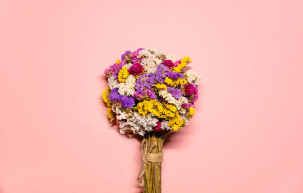 Minimalistické rozložení záběr s kyticí květin uprostřed růžového pozadí. Květiny různých barev: fialové, růžové, žluté a bílé. - Fotografie, Obrázek