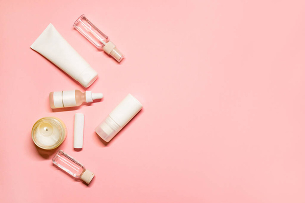 Flat lay shot with a copy space on a pink background with skincare goods: hand cream, deodorant, lipstick, facial serum, essential oil with a lighted candle. - Photo, Image