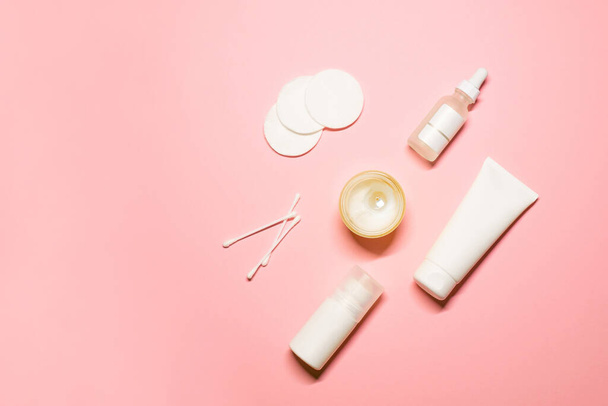 Flache Aufnahmen von Hautpflegeprodukten: Wattepads und -knospen, Gesichtscreme, Serum, Deo und eine Kerze in der Mitte auf rosa Hintergrund. - Foto, Bild