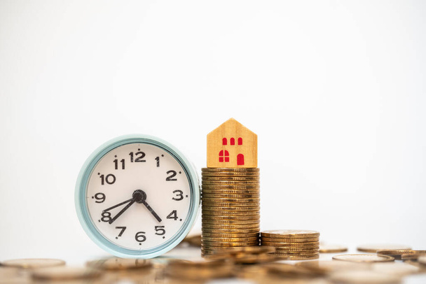 Geld, Business Home Loan und Sparkonzept. Minispielzeug aus Holz auf einem Stapel Münzen mit Vintage-Runduhr auf weißem Hintergrund. - Foto, Bild