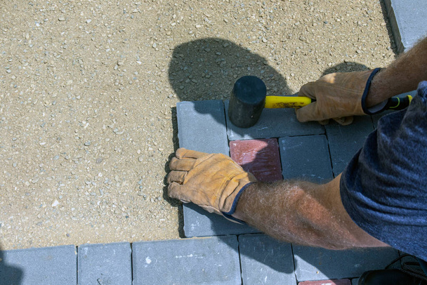 Рукавичний майстер розкладає бруківку шарами. Укладання сірих бетонних тротуарних плит у дворі будинку на піщаному фундаменті
. - Фото, зображення