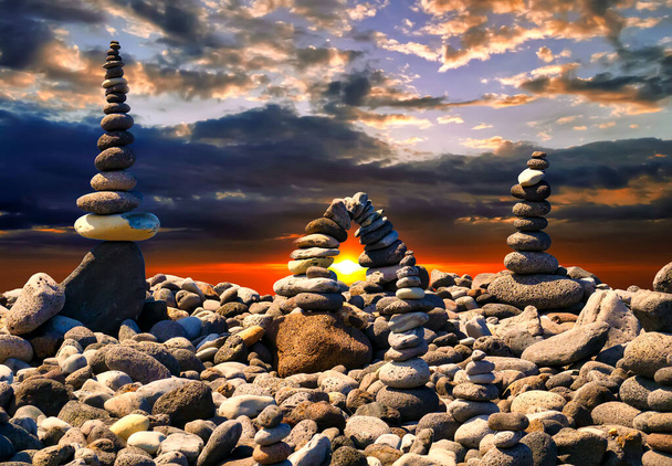 Piedras apiladas en la playa al atardecer. Luz del sol entre las piedras. Pirámide de piedras, concepto zen. - Foto, imagen