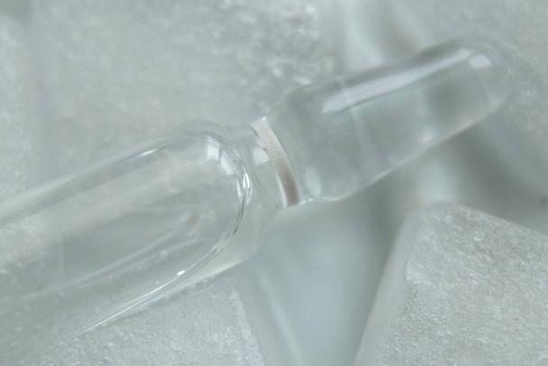 ampulka s vakcínou leží v ledu na bílém pozadí zblízka, vakcinace - Fotografie, Obrázek