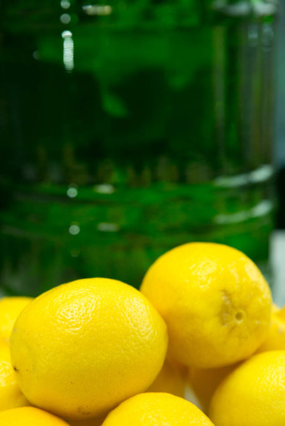 Proces výroby limoncello citrónového likéru doma. Čerstvě omyté citrony na pozadí nádoby s alkoholem. - Fotografie, Obrázek