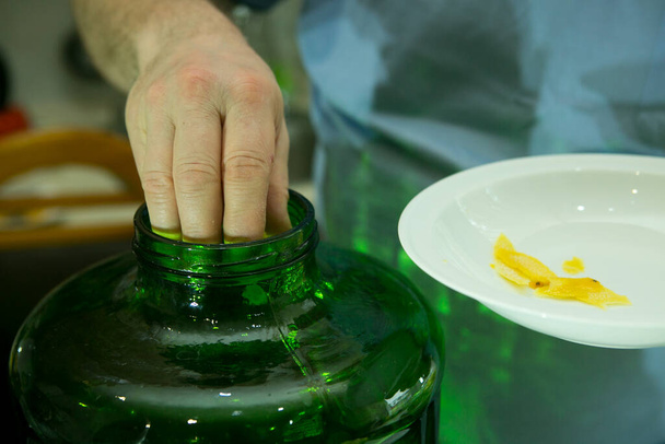 El proceso de hacer licor de limón limoncello en casa. Un hombre añade la ralladura de limón fresca preparada a un recipiente de alcohol. - Foto, imagen