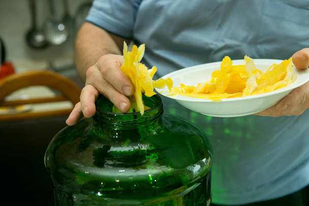 El proceso de hacer licor de limón limoncello en casa. Un hombre añade la ralladura de limón fresca preparada a un recipiente de alcohol. - Foto, imagen