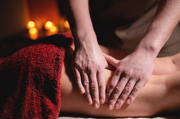 Male masseur doing massage of the knee to a woman patient in a dark room of a spa salon - Zdjęcie, obraz