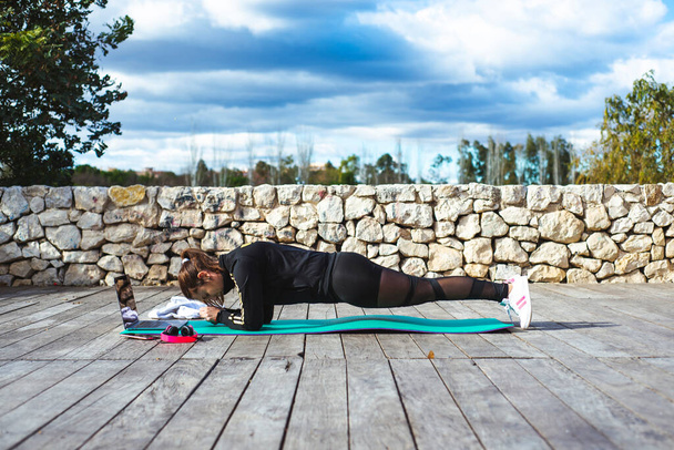 une jeune fille fait des exercices sportifs dans un parc sur le tapis de yoga avec ordinateur portable - Photo, image
