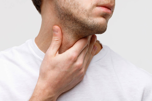 Close up of sick man suffering from throat problems, grey background, isolated. Thyroid gland, painful swallowing, pharyngitis, laryngeal swelling concept. Inflammation of the upper respiratory tract - Photo, Image