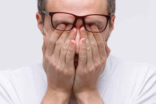 Schläfriger Mann mit Brille reibt sich die Augen, fühlt sich müde nach der Arbeit am Laptop, isoliert auf weißem Hintergrund. Überlastung, Erschöpfung, chronische Müdigkeit, psychischer Stress, Schlafmangel - Foto, Bild